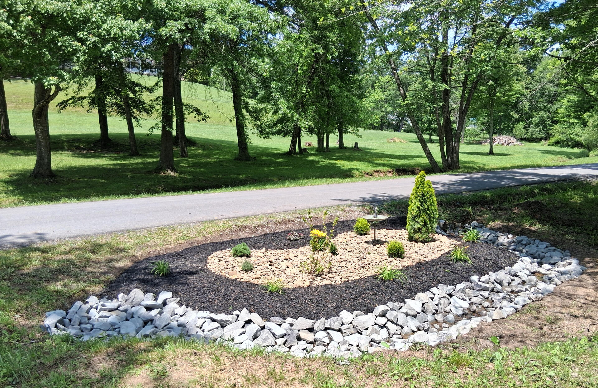 Roadside Gardenbed Installation, Greater Beckley Area, West Virginia Newly designed and installed luxury landscaped garden bed with large drainage rocks, black mulch, designer river stone, and designer plants with copper buddha bird bath in Fairdale, WV 25839